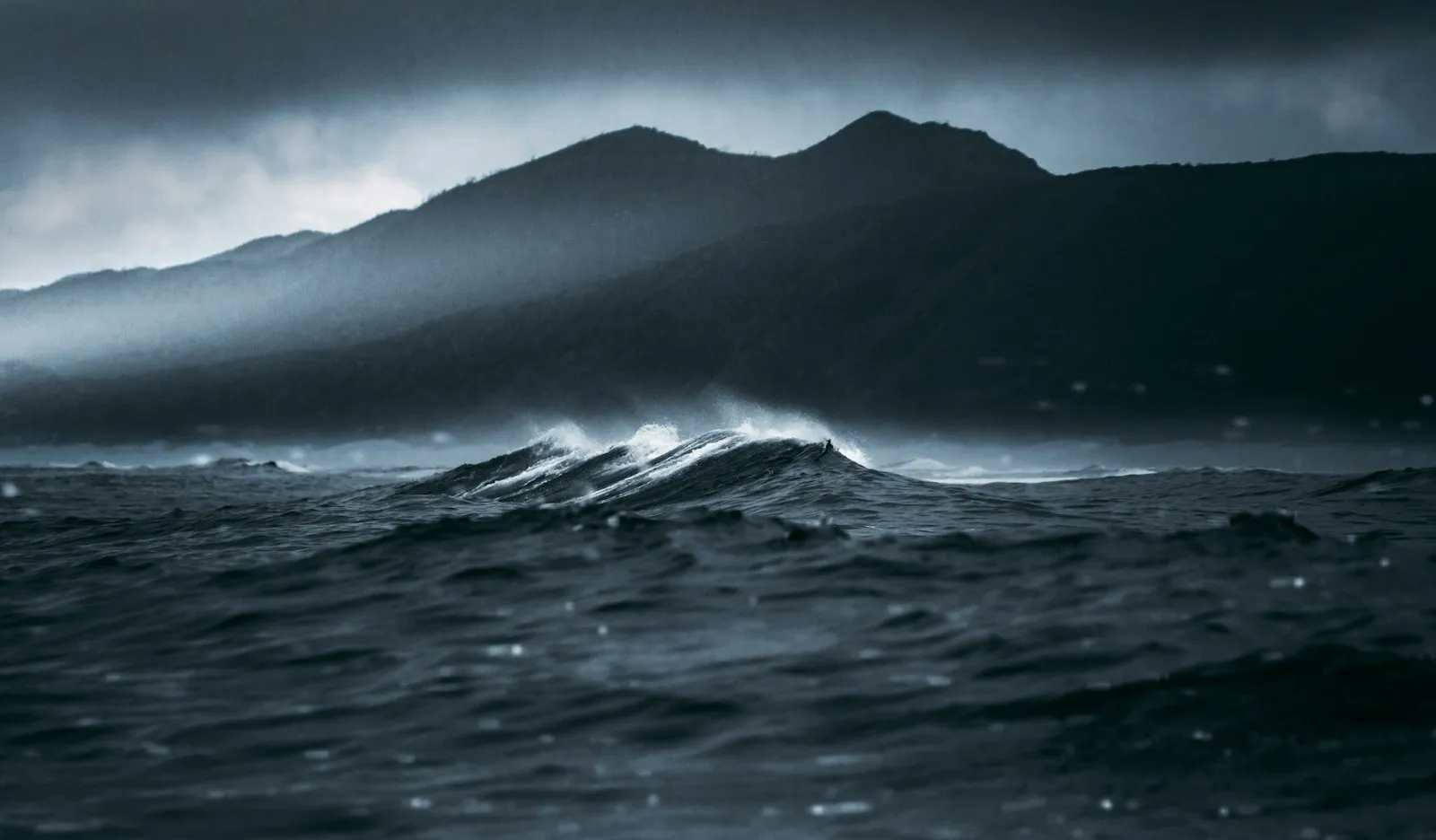 Hoge golven en schuim slaan tegen een donkere, onstuimige kustlijn tijdens een storm.